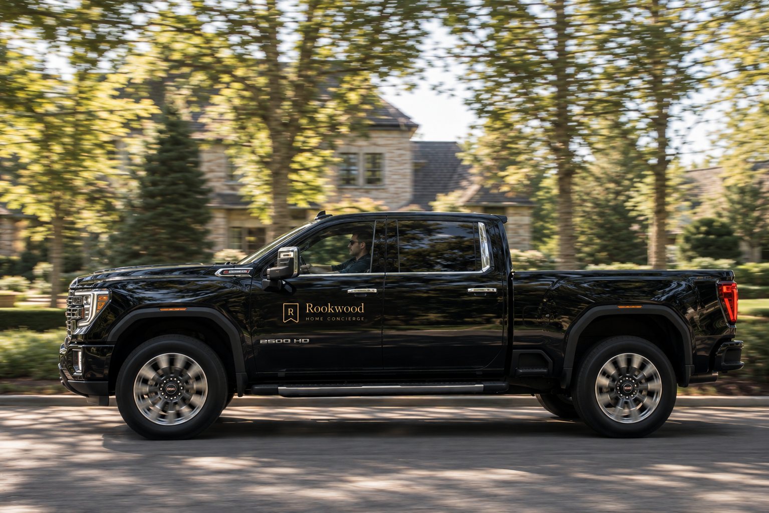 A black Rookwood Home Concierge truck driving down a tree-lined residential street